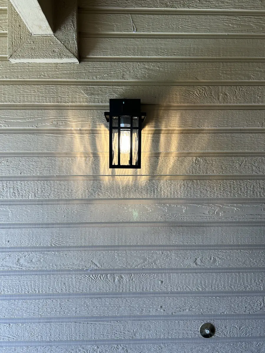 Black wall lantern lit against painted wood siding
